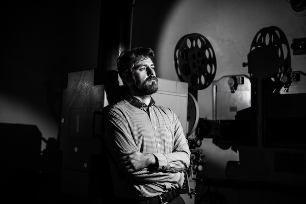 beautiful hipster man standing near a film projector in the room projectionist